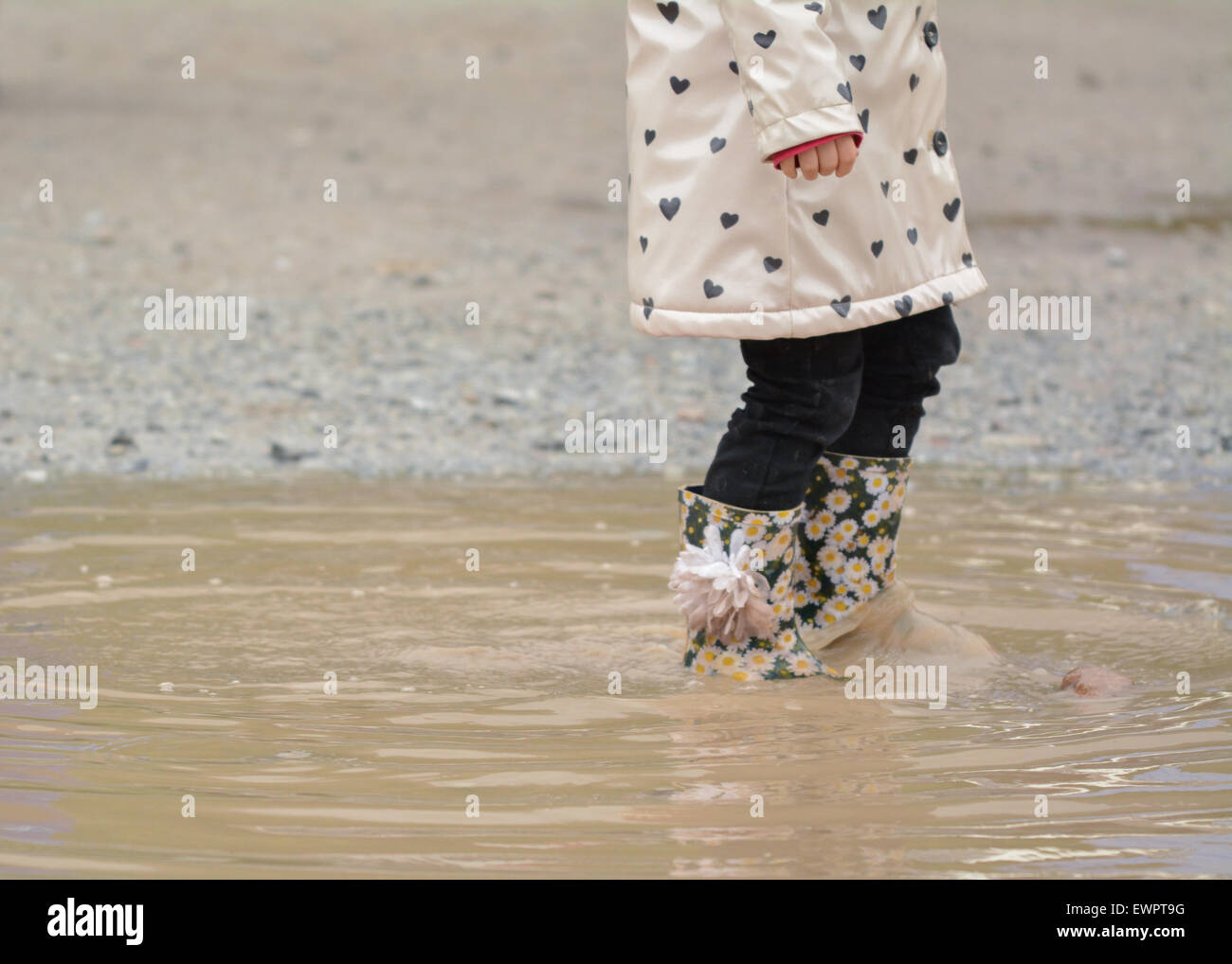 junge Mädchen tragen geblüht Gummistiefel zu Fuß durch schlammige Pfütze Stockfoto