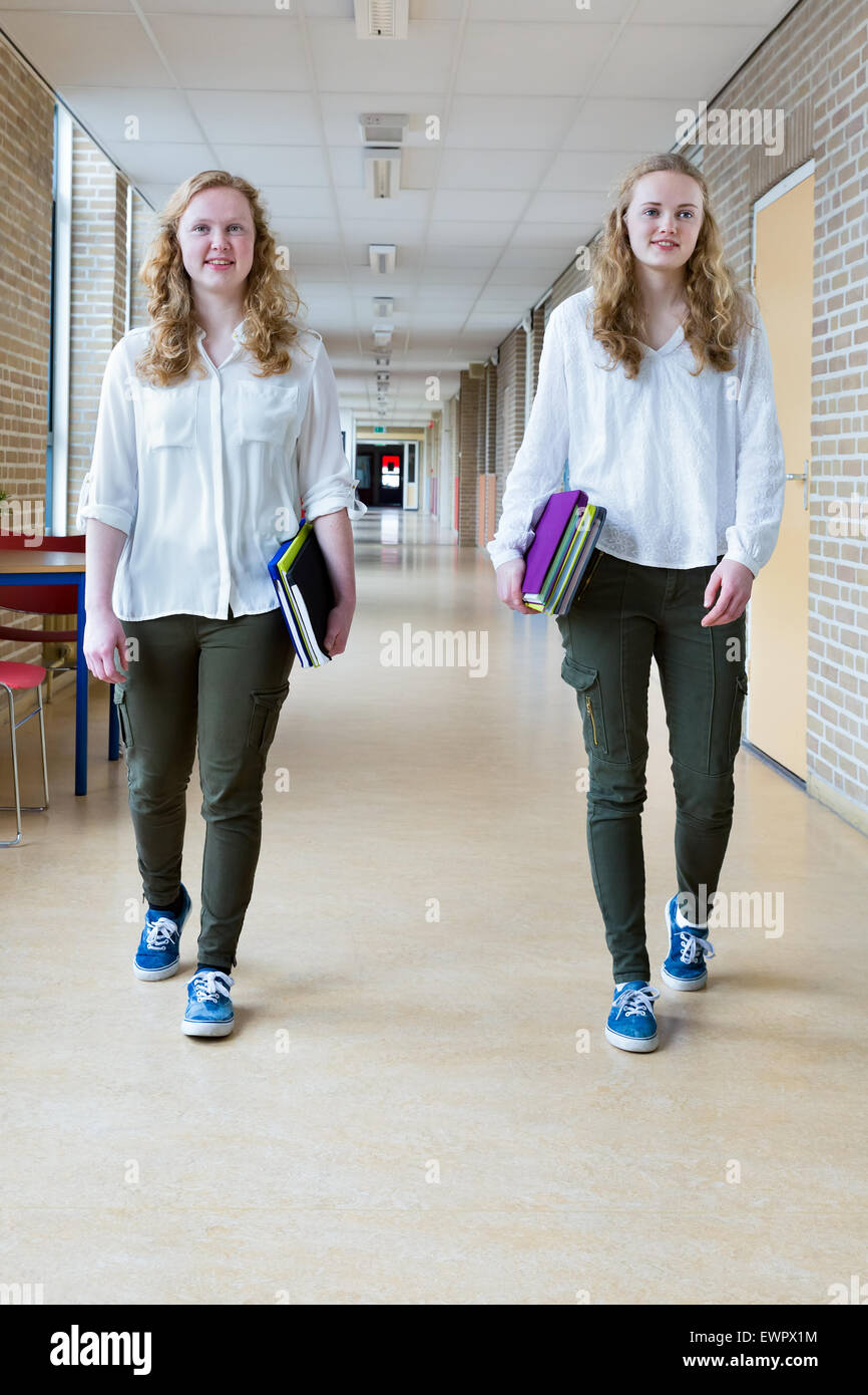 Zwei kaukasische Mädchen im Teenageralter zu Fuß auf lange Schule Flur tragen Textbücher Stockfoto