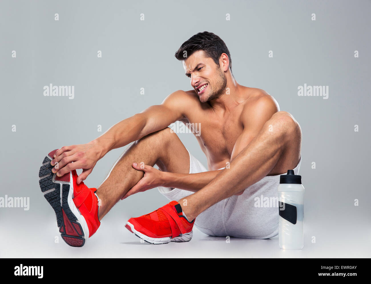 Porträt eines Mannes Fitness mit Fußschmerzen auf grauem Hintergrund Stockfoto