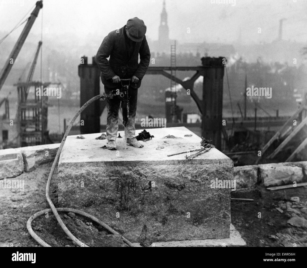 Ein Arbeiter, Bohren von Löchern in eines der Bedstones auf die Gateshead Widerlager für die Lager der Stahlträger des neuen Tyne Bridge. Die Firders startet von dem Widerlager über Church Street pm die Stahlsäulen im Hintergrund zu sehen. Tyne and Wear, 29. Dezember 1926. Stockfoto