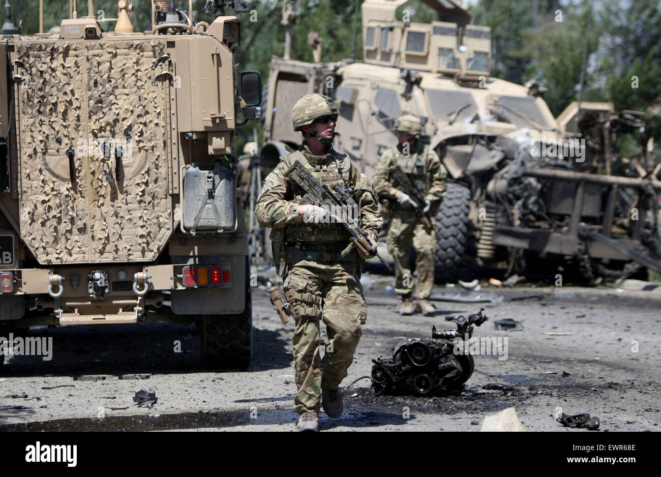 Kabul, Afghanistan. 30. Juni 2015. Ausländische Soldaten spazieren Sie durch ein zerstörtes Militärfahrzeug nach einem Bombenanschlag in Kabul, Afghanistan, 30. Juni 2015 Selbstmord-Auto. Mindestens eine Person wurde, bestätigten Toten und 22 weitere wurden verletzt, als ein Selbstmordattentäter seinen Sprengstoff beladenen Wagen neben einem Konvoi der NATO-geführten entschlossene Unterstützung (RS)-Mission in der afghanischen Hauptstadt Kabul am Dienstag, Sprecher für Innenministerium sprengte, sagte Sediq Sediqi. © Ahmad Massoud/Xinhua/Alamy Live-Nachrichten Stockfoto