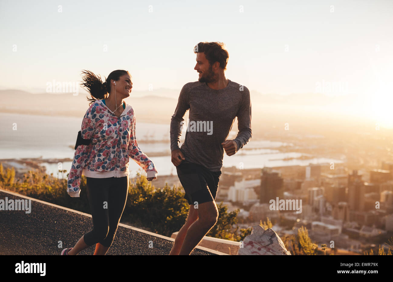 Junges Paar laufen zusammen im Freien. Glücklicher junger Mann und Frau, Joggen auf Landstraße bei Sonnenaufgang. Zwei Menschen, die genießen mo Stockfoto