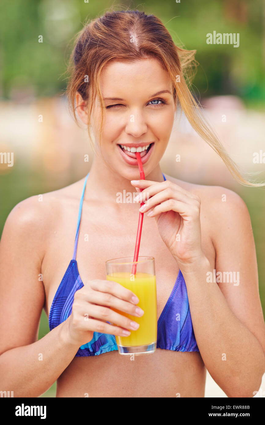 Glückliche Frau in Bikini trinken Orangensaft und zwinkert Stockfoto