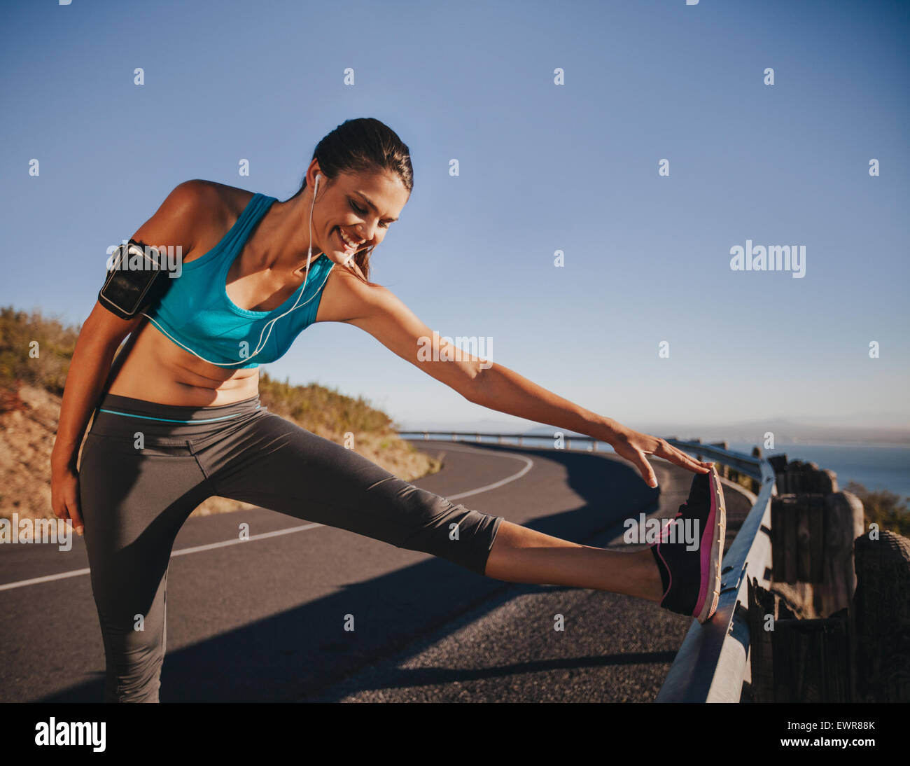 Sportliche Frau dehnen ihr Bein auf einem Geländer vor im freien laufen. Sportlerin, immer bereit für einen Lauf. Stockfoto