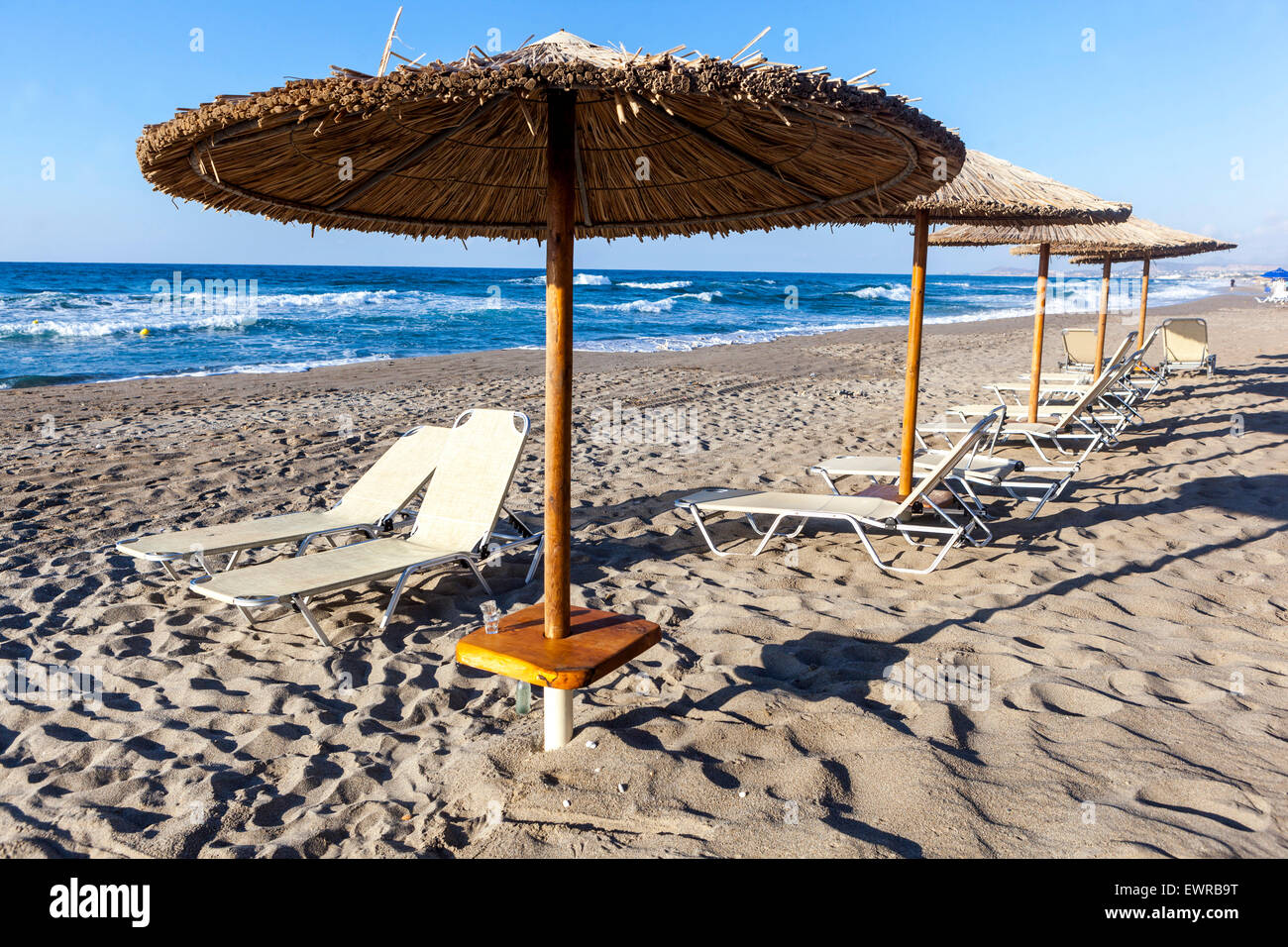 Stroh Strand Sonnenschirme und Liegestühle am leeren Strand von Rethymno, Kreta Strand Griechenland Europa Stockfoto