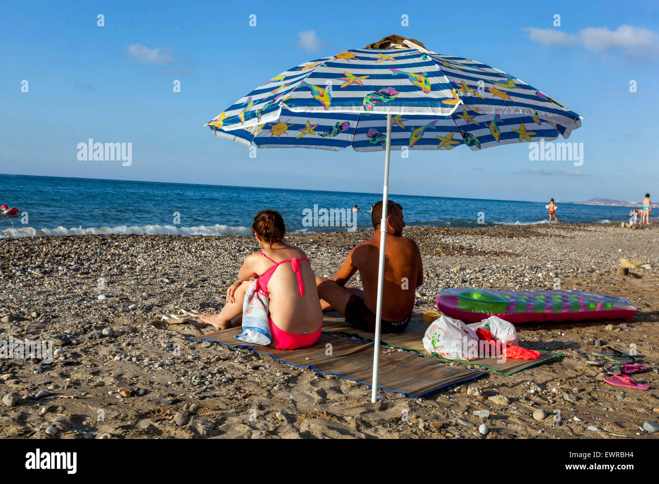 Pärchen, die unter dem Sonnenschirm am Strand von Rethymno, Kreta, sitzen, Griechenland Urlauber Stockfoto