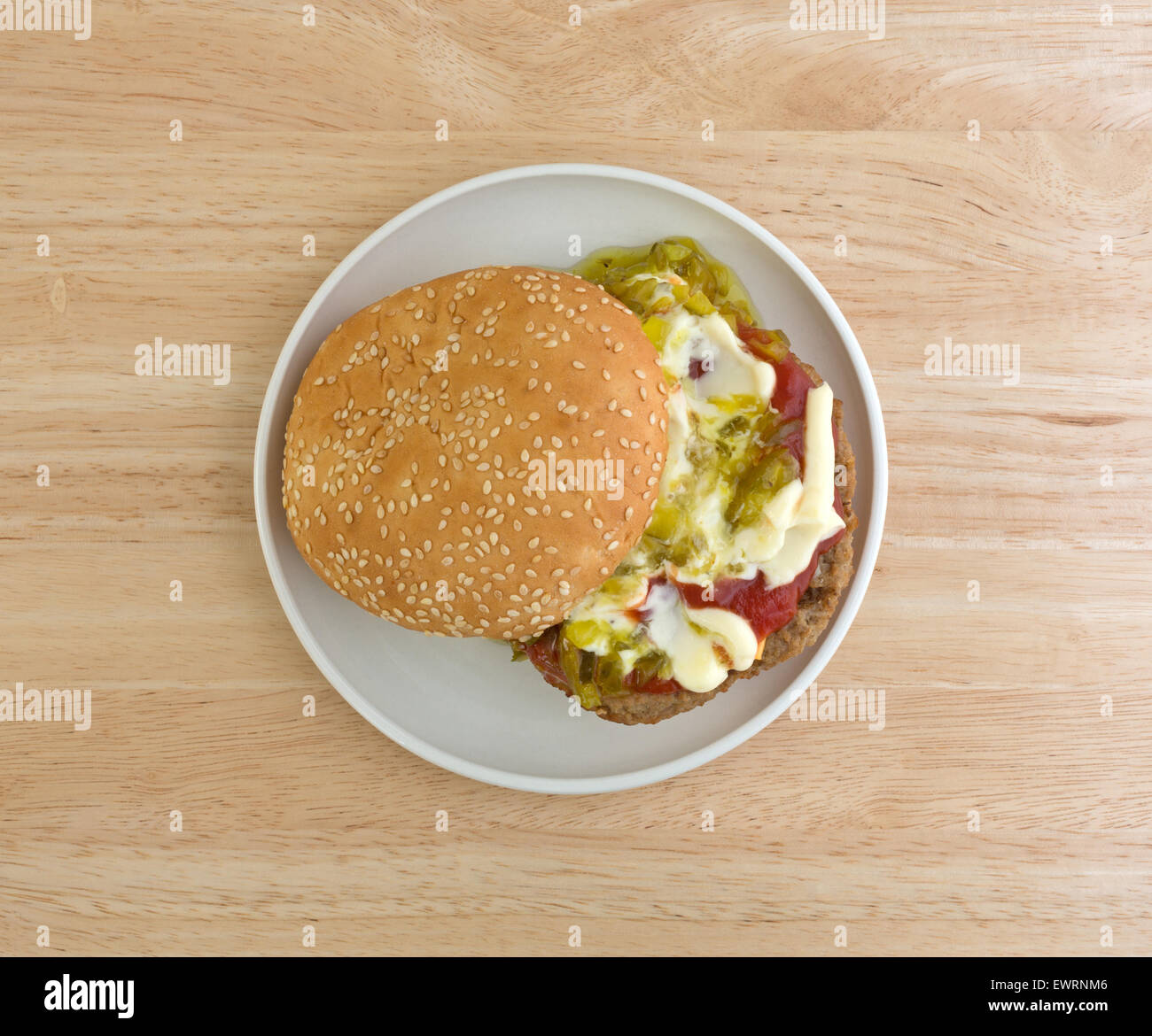 Draufsicht auf einen Cheeseburger mit Sesam Brötchen sowie Mayonnaise, Ketchup und lustvoll auf einen kleinen Teller auf Holztisch. Stockfoto