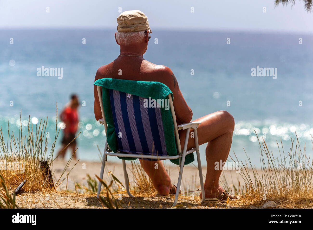 Senior Mann in einem Klappstuhl, der das Meer beobachtet. Der Strand von Plakias, Südkreta, Griechenland. Sonnenbaden Senior am Strand Sonne Wohlbefinden Stockfoto