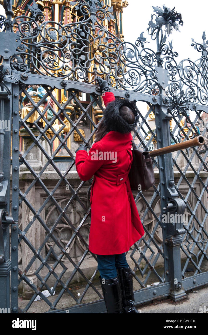 Eine Frau in einem roten Mantel Spinnen einen Messingring im Schöner Brunnen, Nürnberg viel Glück bringen Stockfoto