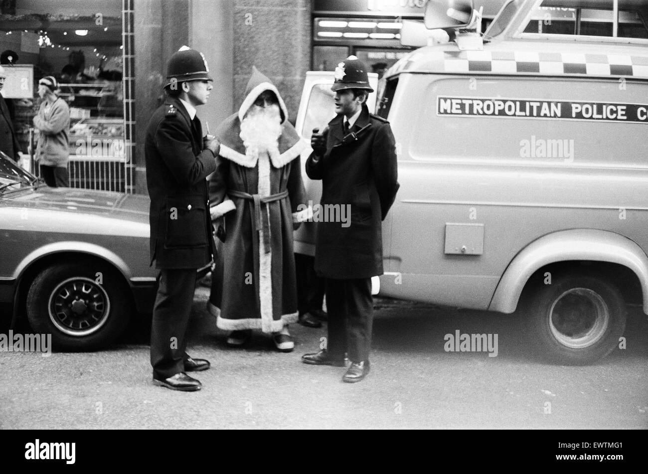 Polizisten sprechen an den Weihnachtsmann außerhalb das Kaufhaus Harrods in London. Santa bot mit Passanten darstellen, während ein Kollege Fotos machten. Polizei verhaftete ihn wegen Behinderung. 19. Dezember 1982. Stockfoto