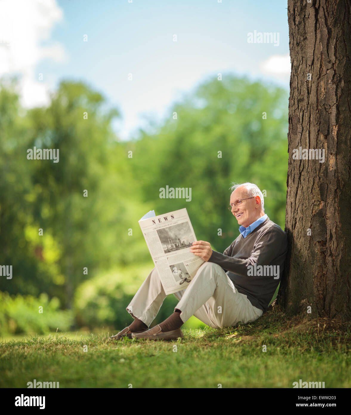 Entspannte senior Gentleman, lesen eine Zeitung auf dem Rasen im Park sitzen und genießen einen schönen sonnigen Sommertag Stockfoto