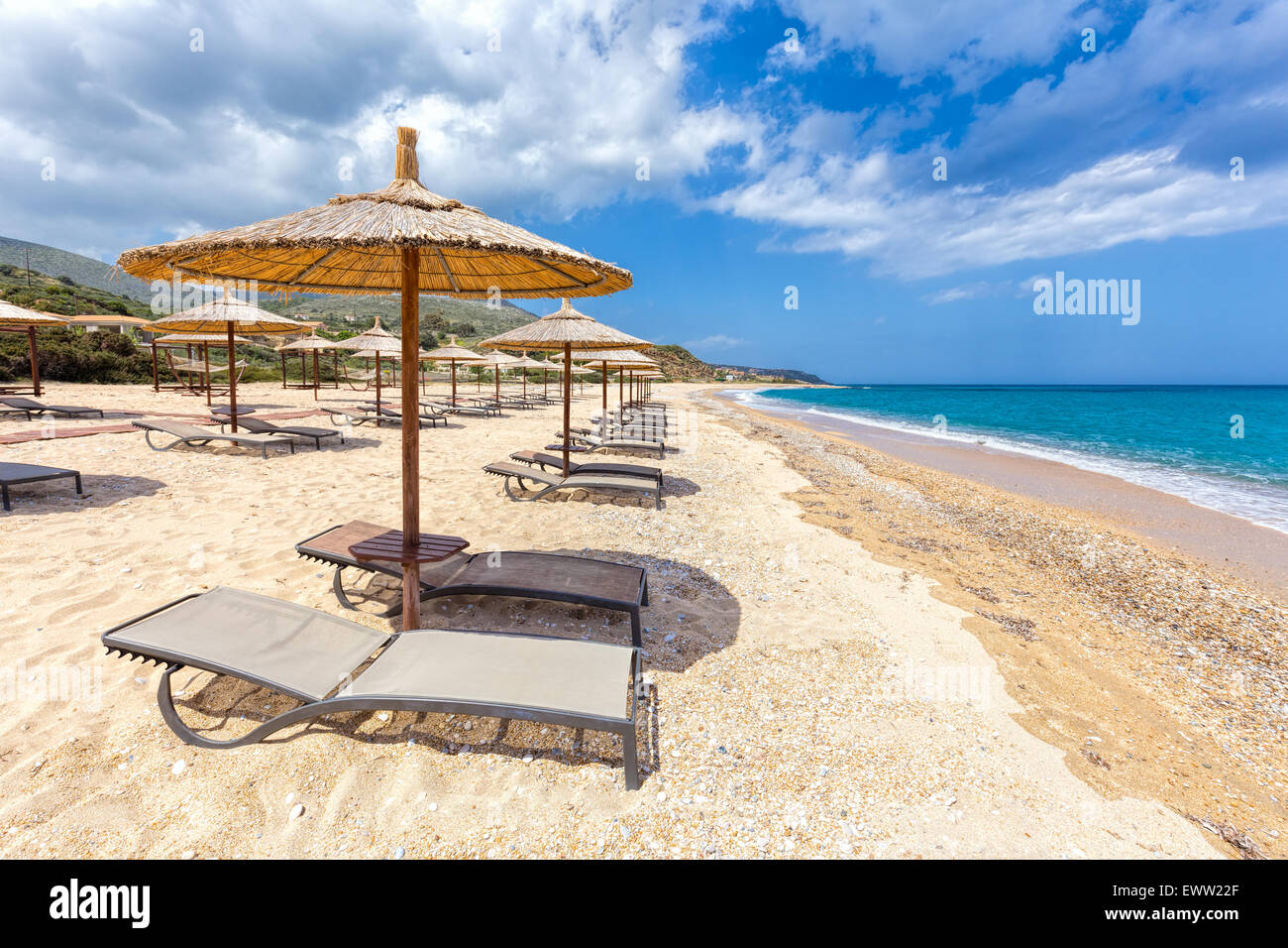 Sonnenschirme in Reihen für Schatten am Sandstrand an der Küste mit blauen Meer in Griechenland Stockfoto