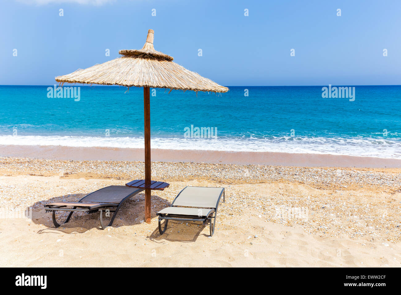 Reed-Sonnenschirm mit 2 liegen am Strand in der Nähe der Küste des blauen Meeres in Griechenland Stockfoto