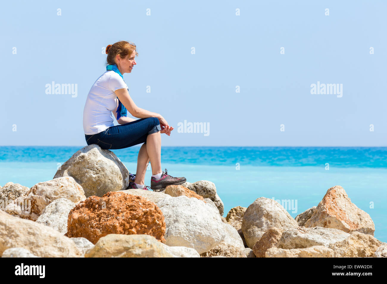 Mittleren Alter Europäerin als Tourist auf Felsen sitzend mit blauen Meereshorizont, die Aussicht genießen Stockfoto