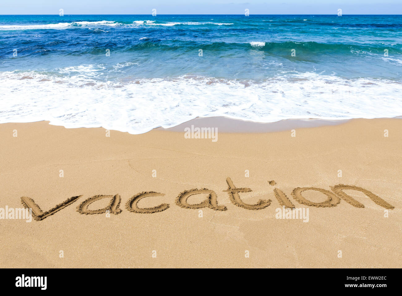 Wort Urlaub geschrieben in Sandstrand an der Küste mit blauem Meer und Wellen Stockfoto