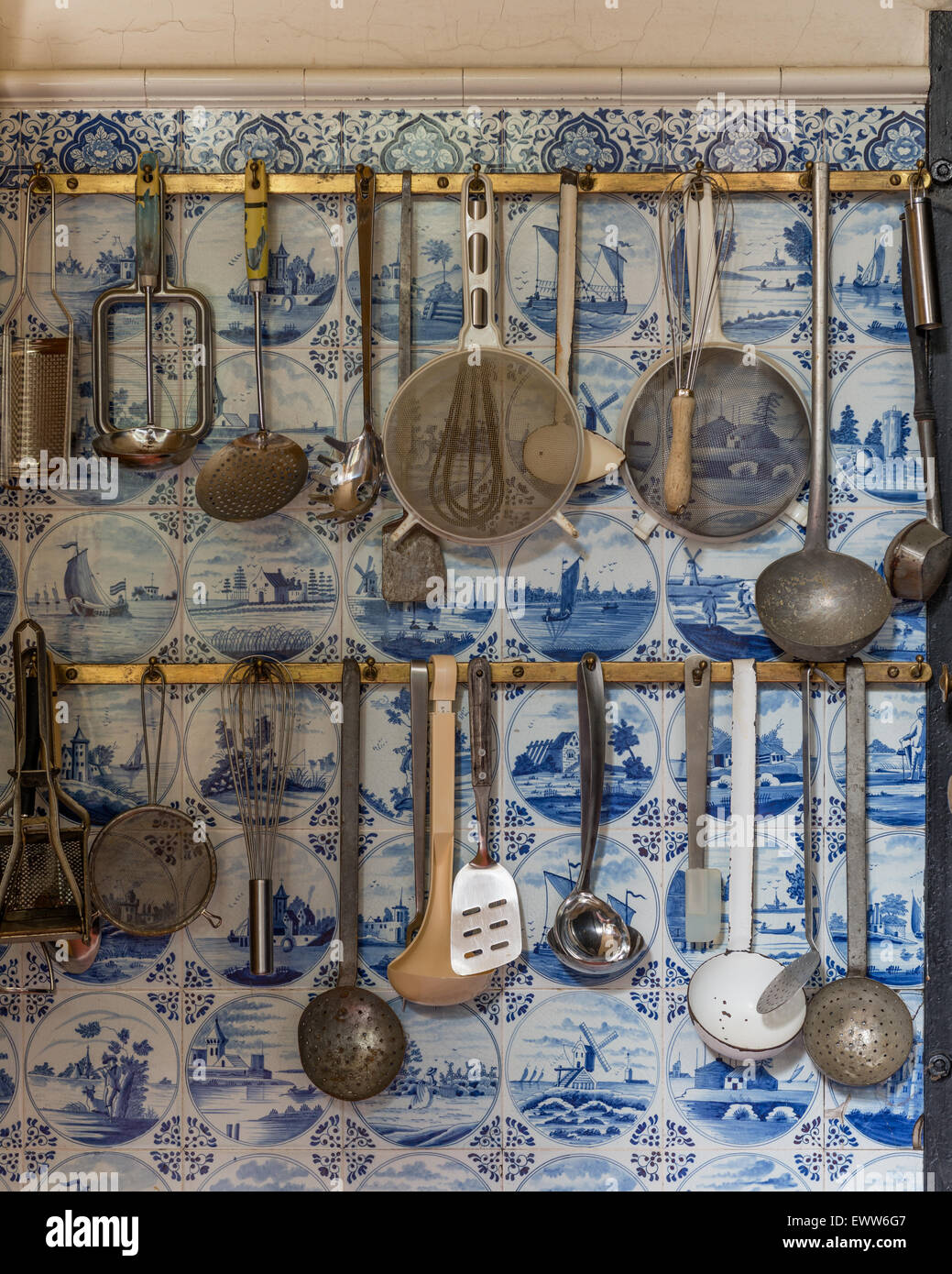 Küchenutensilien aufgehängt am Rack mit Delfter Kacheln hinter Stockfoto