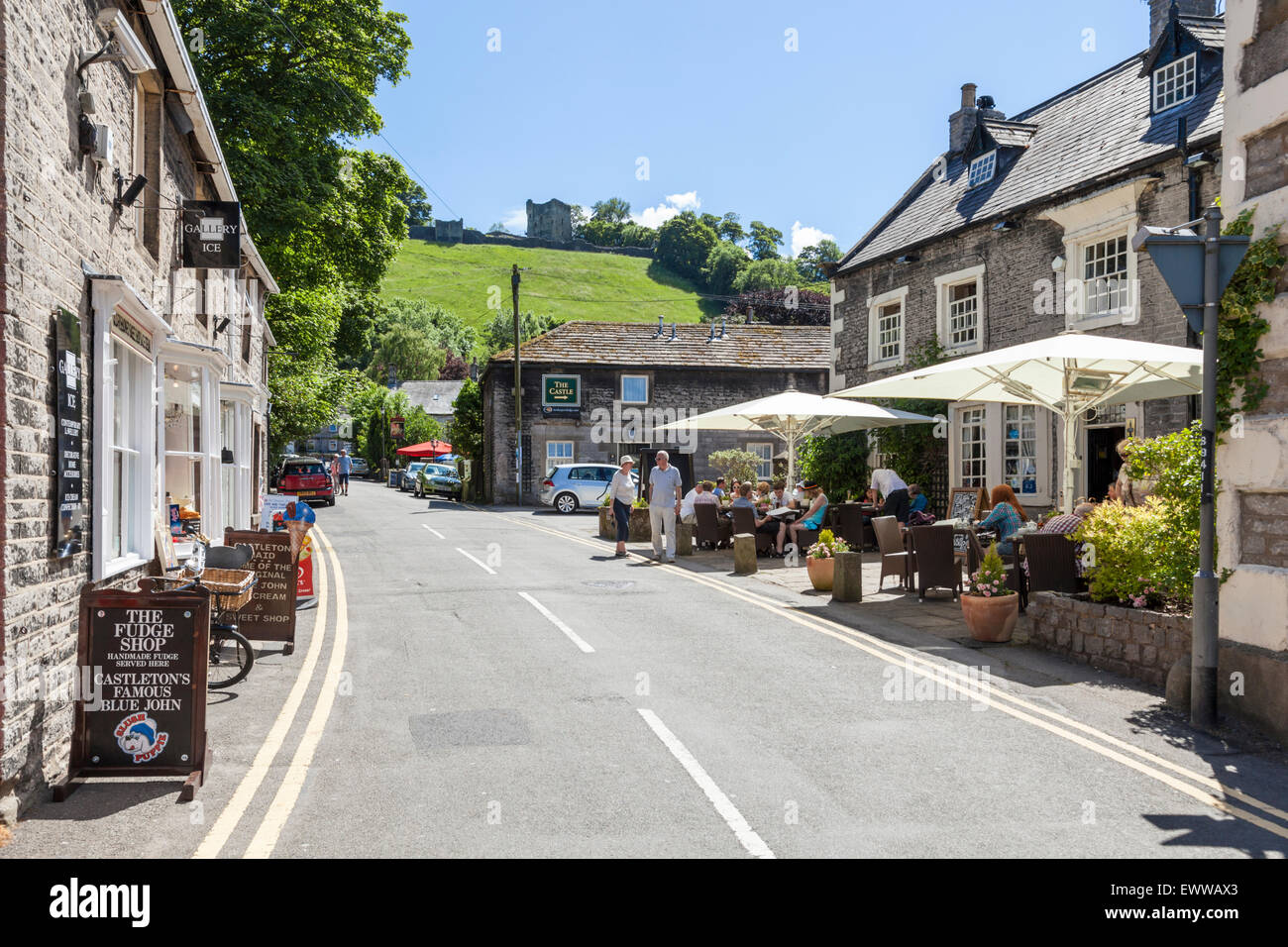 Geschäfte und eine Kneipe in Castleton mit Peveril Castle auf dem Hügel mit Blick auf das Dorf im Sommer, Derbyshire, Peak District National Park, England, Großbritannien Stockfoto