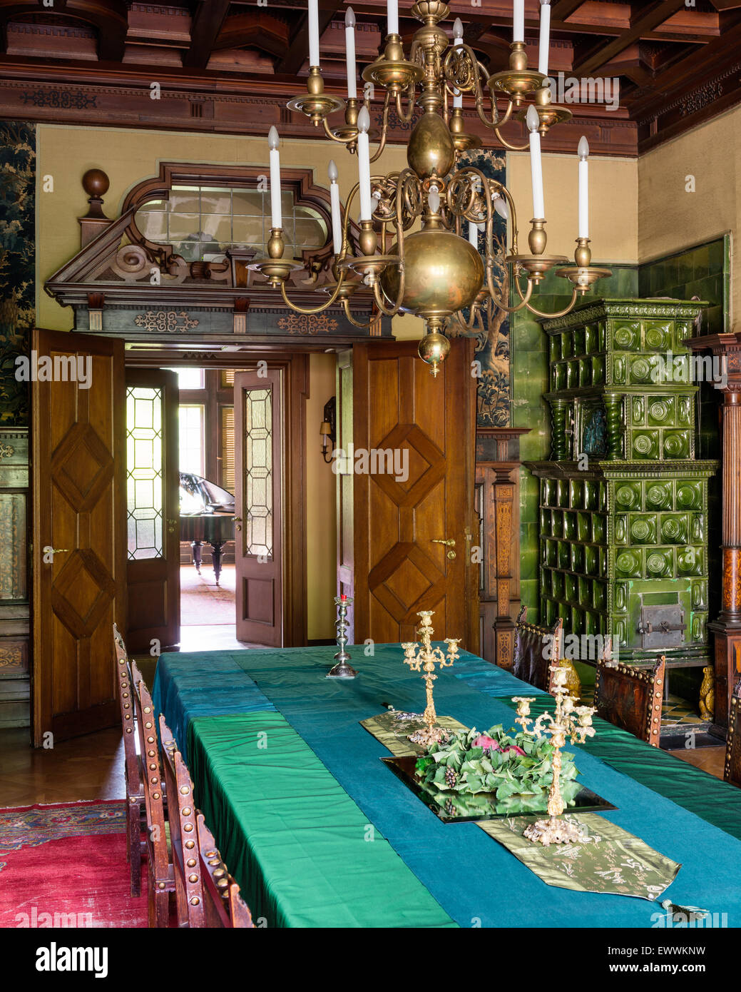 Kronleuchter aus Messing über lange Esstisch im Zimmer mit grünen Kachelofen Stockfoto
