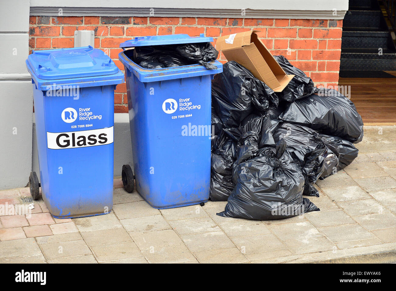 Blaue Wheelie-Kästen und schwarzen Plastiktüten mit Müll vor einem Café. Stockfoto