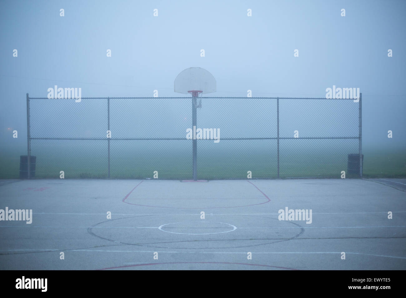 Eine neblige Stadtlandschaft in der Abenddämmerung auf einem Basketballfeld in einem Park. Stockfoto