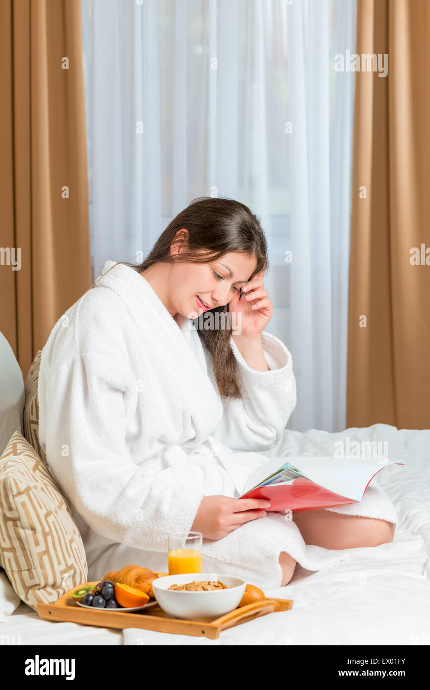 weibliche Frühstück am Morgen und einer Zeitschrift auf dem Bett Stockfoto