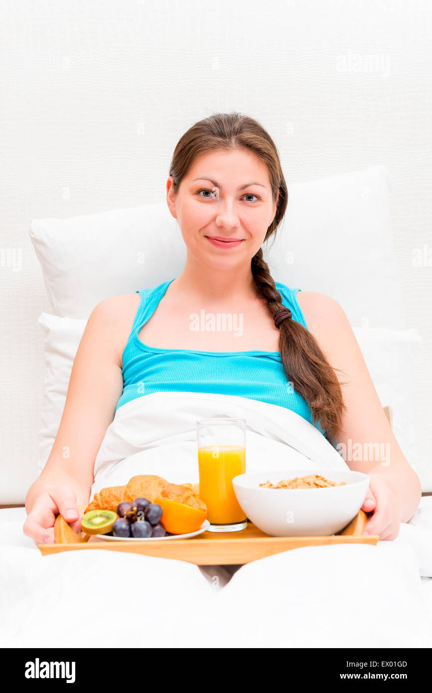 eine Frau mit einem Tablett mit Frühstück im Bett am Morgen Stockfoto