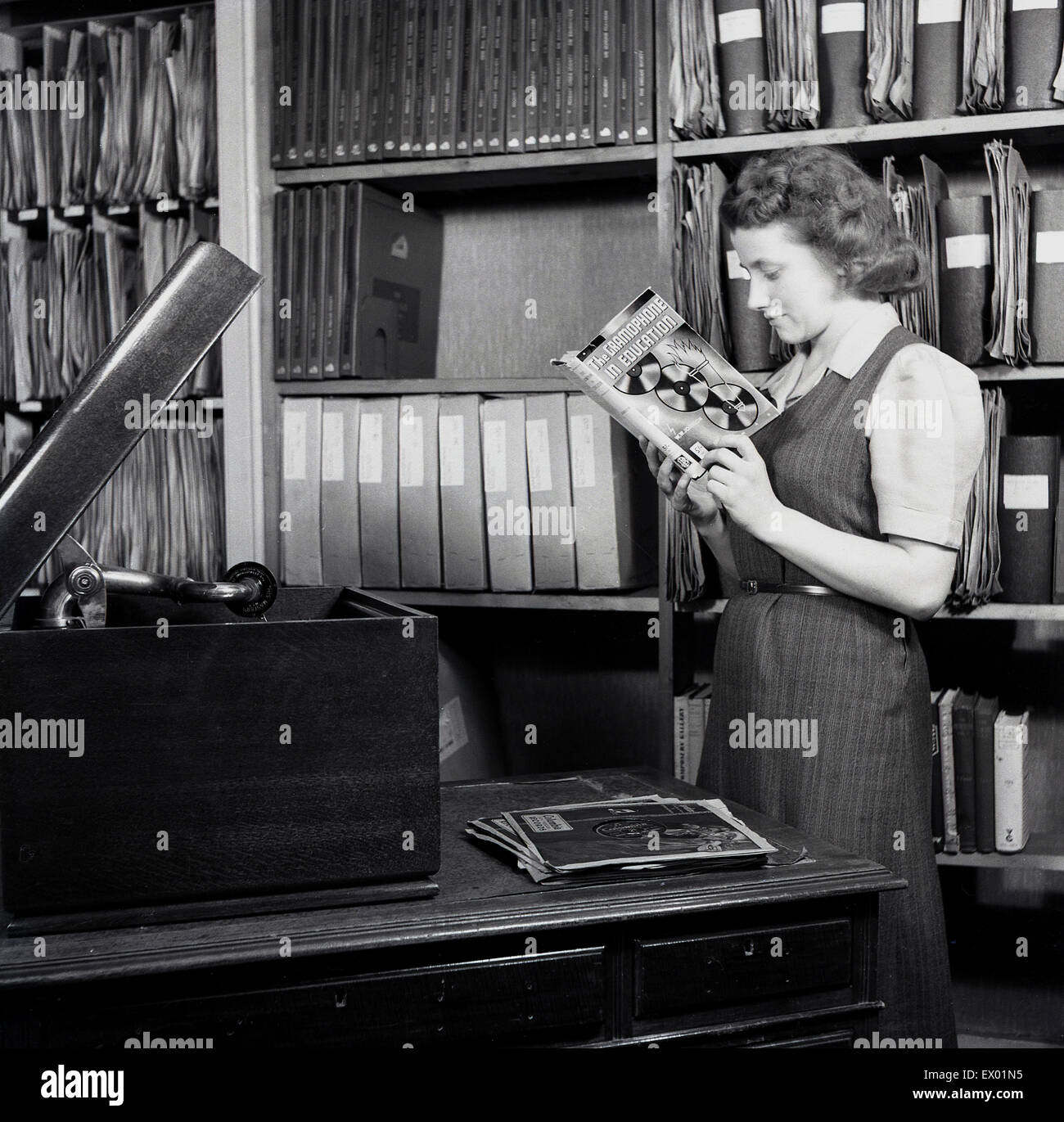 Historisches, 1950er Jahre, junge Dame in der Bibliothek einen Katalog zu studieren und hören von Schallplatten. Stockfoto