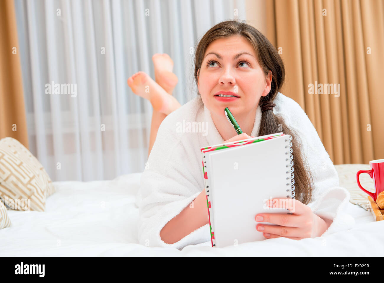 Attraktive Brünette mit einem Notizbuch und Stift auf dem Bett Stockfoto