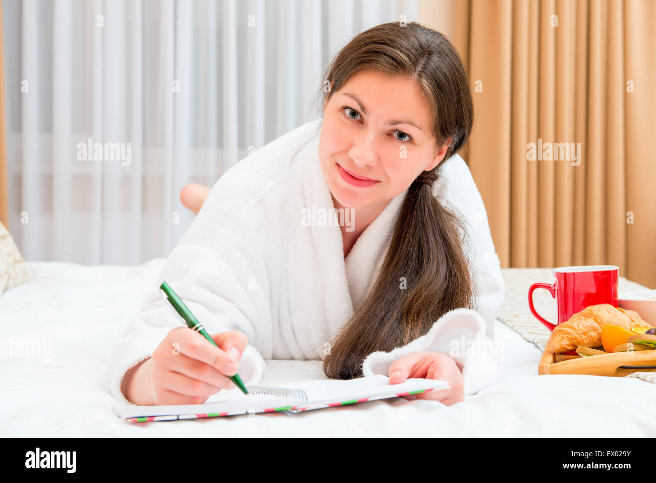 Frau macht sich Notizen in einem Notizbuch auf dem Bett liegend Stockfoto