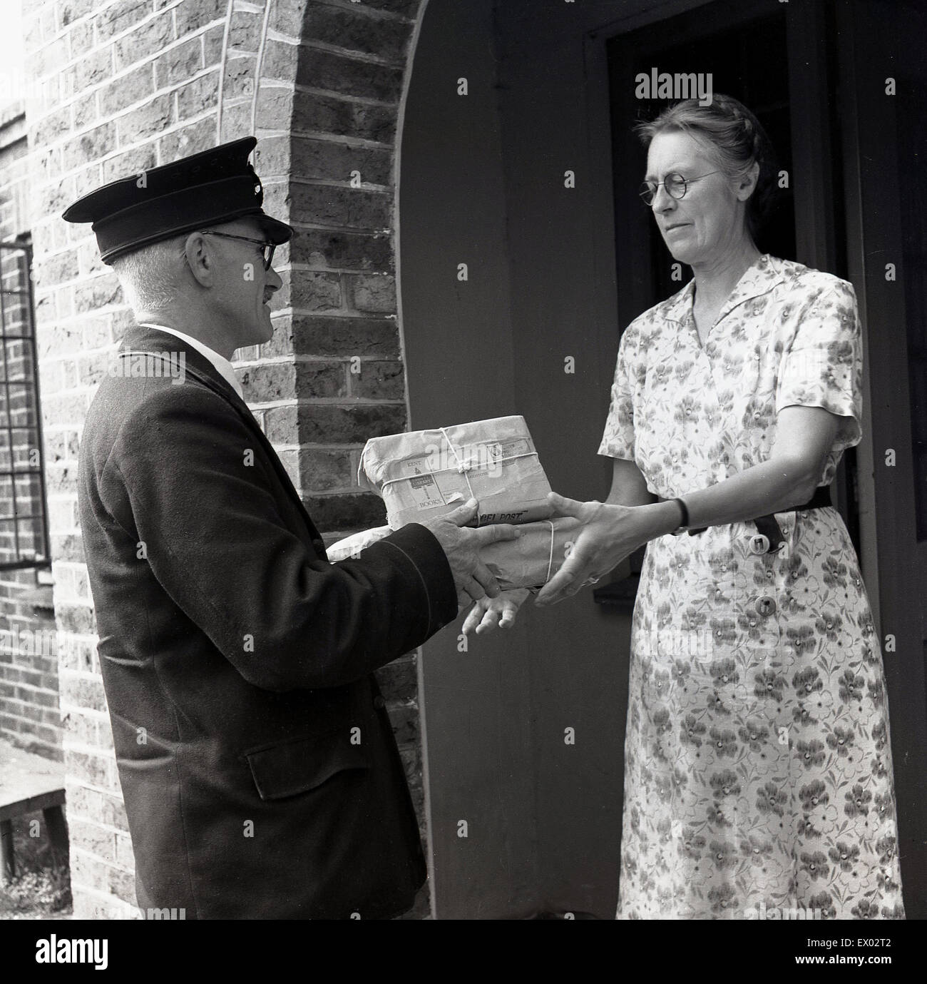 England der 1950er Jahre. Frau am Eingang zum Haus dauert die Lieferung von zwei kleinen Parzellen in diesem historischen Bild von J Allan Cash. Stockfoto