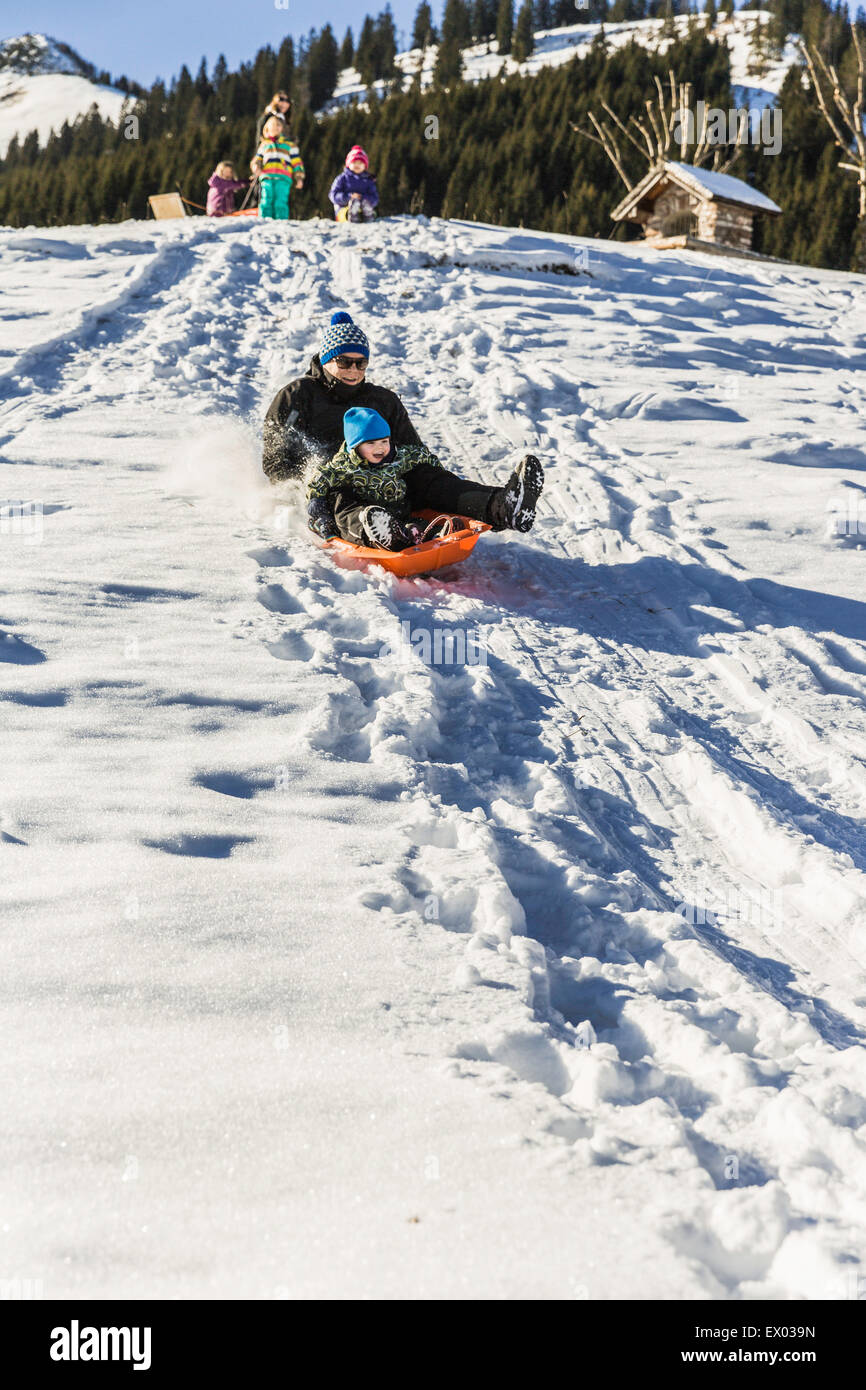 Vater und Sohn fahren Schlitten Schnee bedeckten Hang hinunter, Achenkirch, Tirol, Österreich Stockfoto