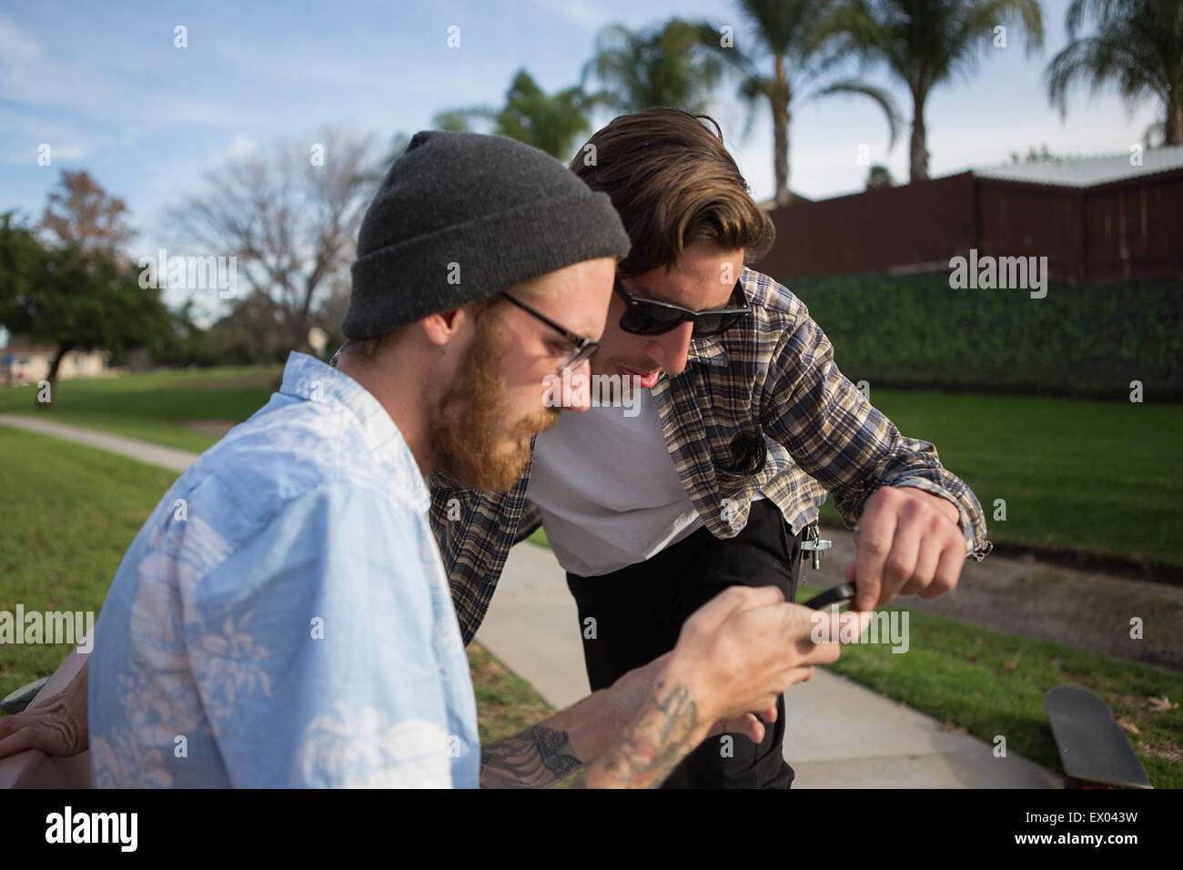 Zwei junge männliche Freunde betrachten Smartphone auf suburban Bank Stockfoto