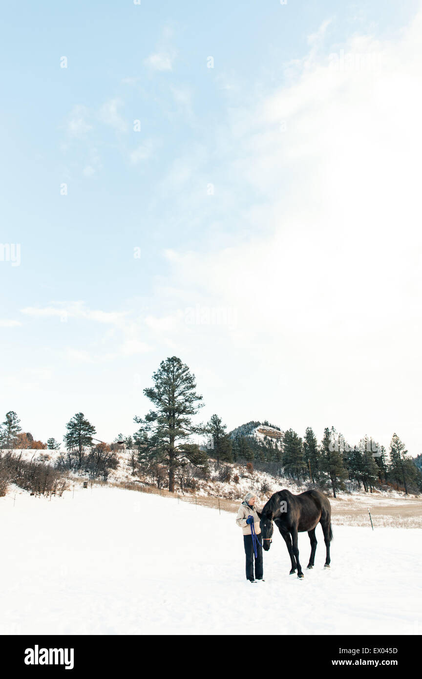 Ältere Erwachsene Frau stehend mit Pferd in Schneelandschaft Stockfoto
