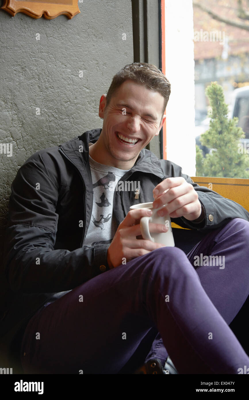 Junger Mann sitzt im Café Fenster Sitz lachen Stockfoto