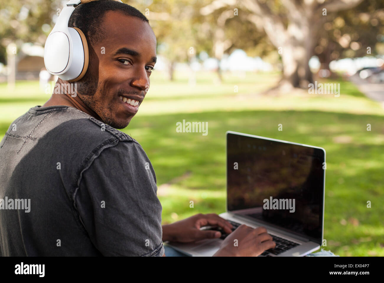 Junger Mann, draußen, tragen von Kopfhörern und mittels Laptop, über die Schulter schauen Stockfoto