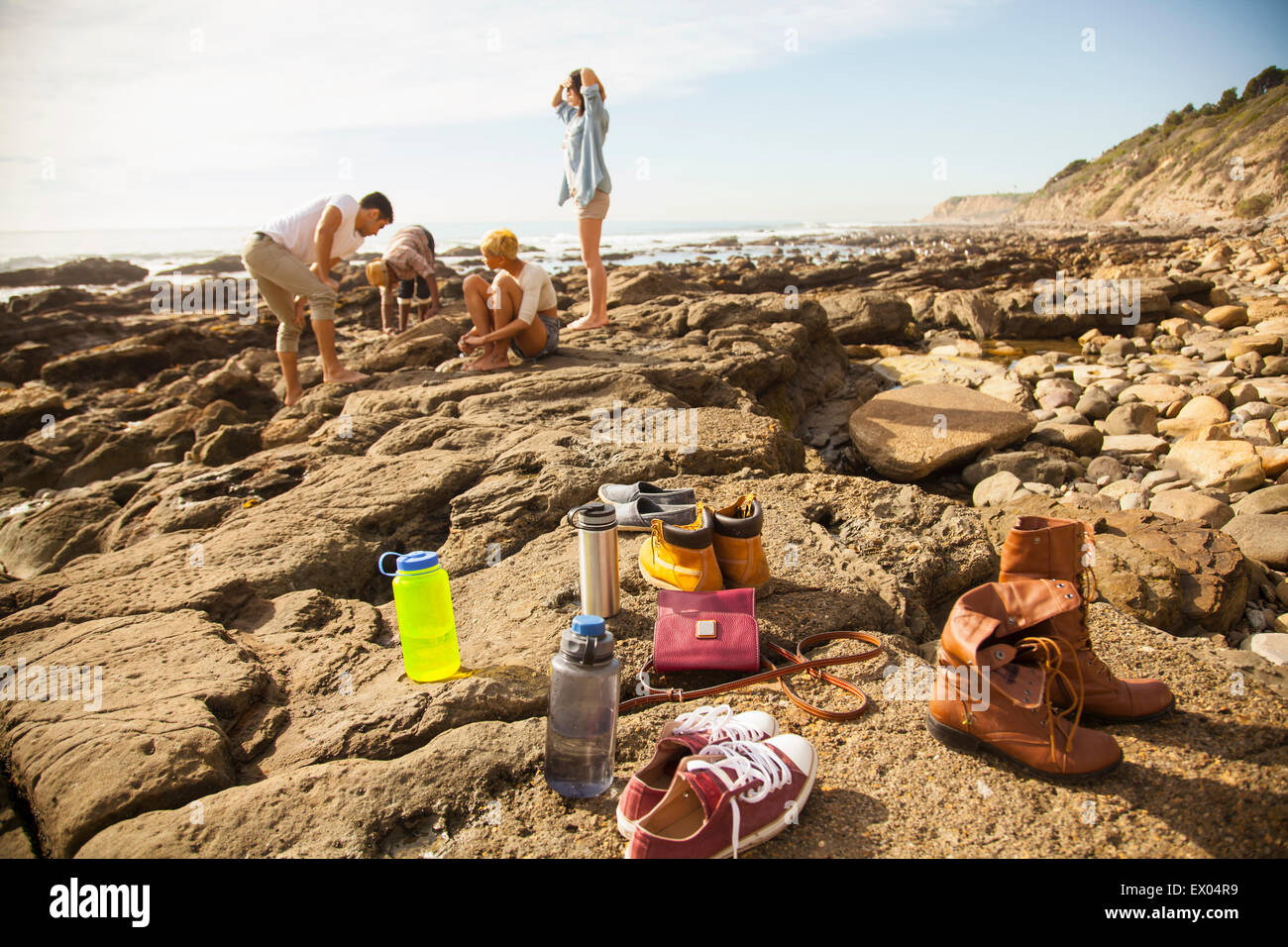 Gruppe von Freunden, die Fels-Pools zu erkunden, am Strand, Schuhe und Gegenstände im Vordergrund Stockfoto