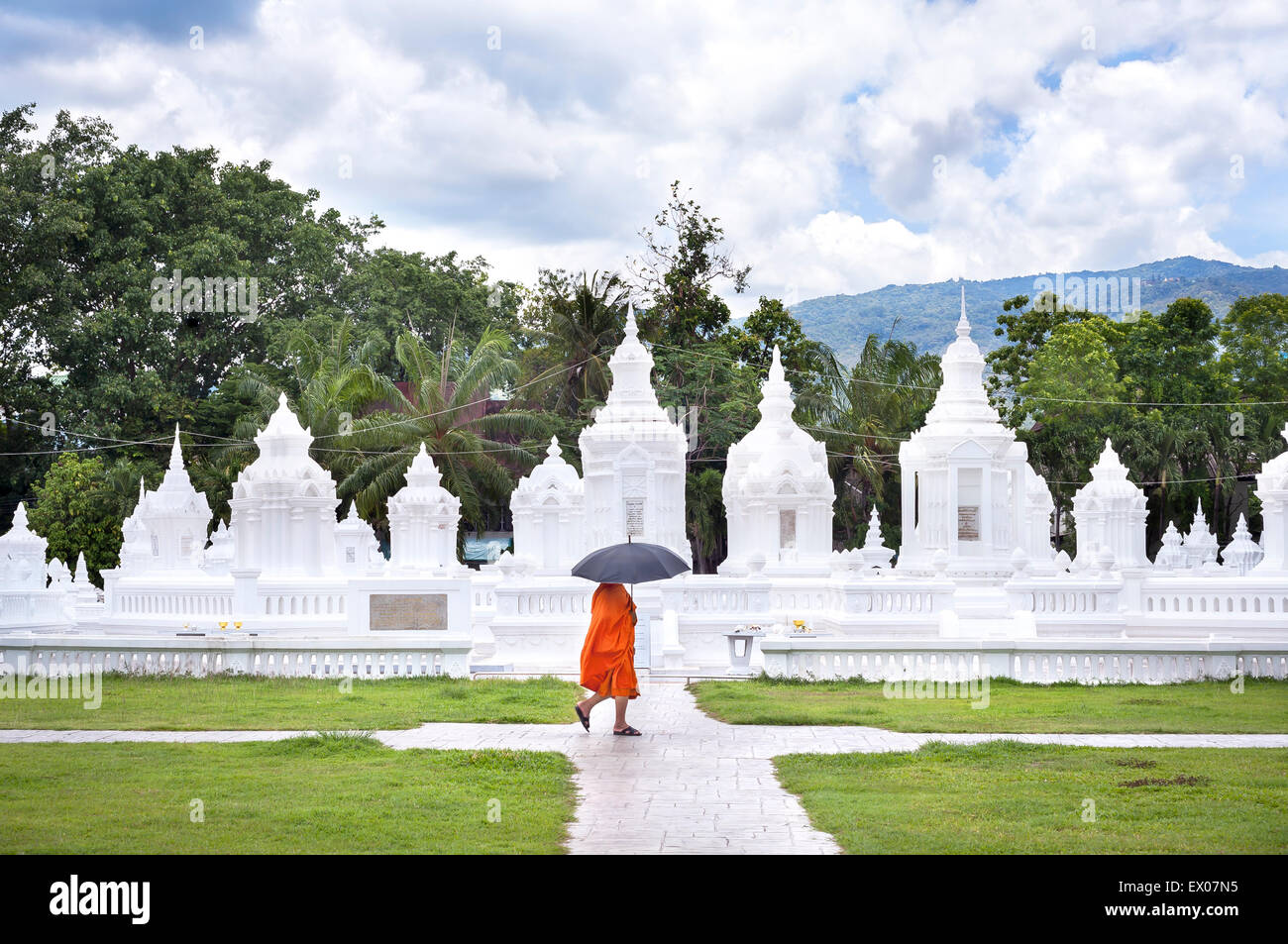 Ein Regenschirm-tragenden Mönch geht vorbei an den charakteristischen weißen Chedis des Wat Suan Dok, Chiang Mai, Thailand Stockfoto