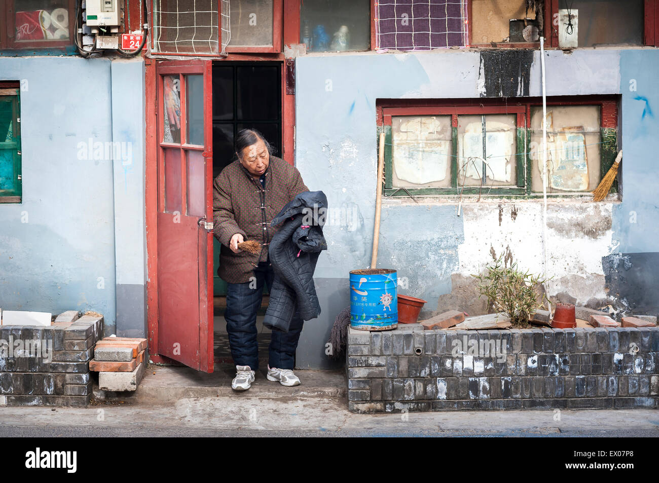 Alte lokale Frau Reinigung einen Mantel außerhalb ihrer Hutong home Stockfoto