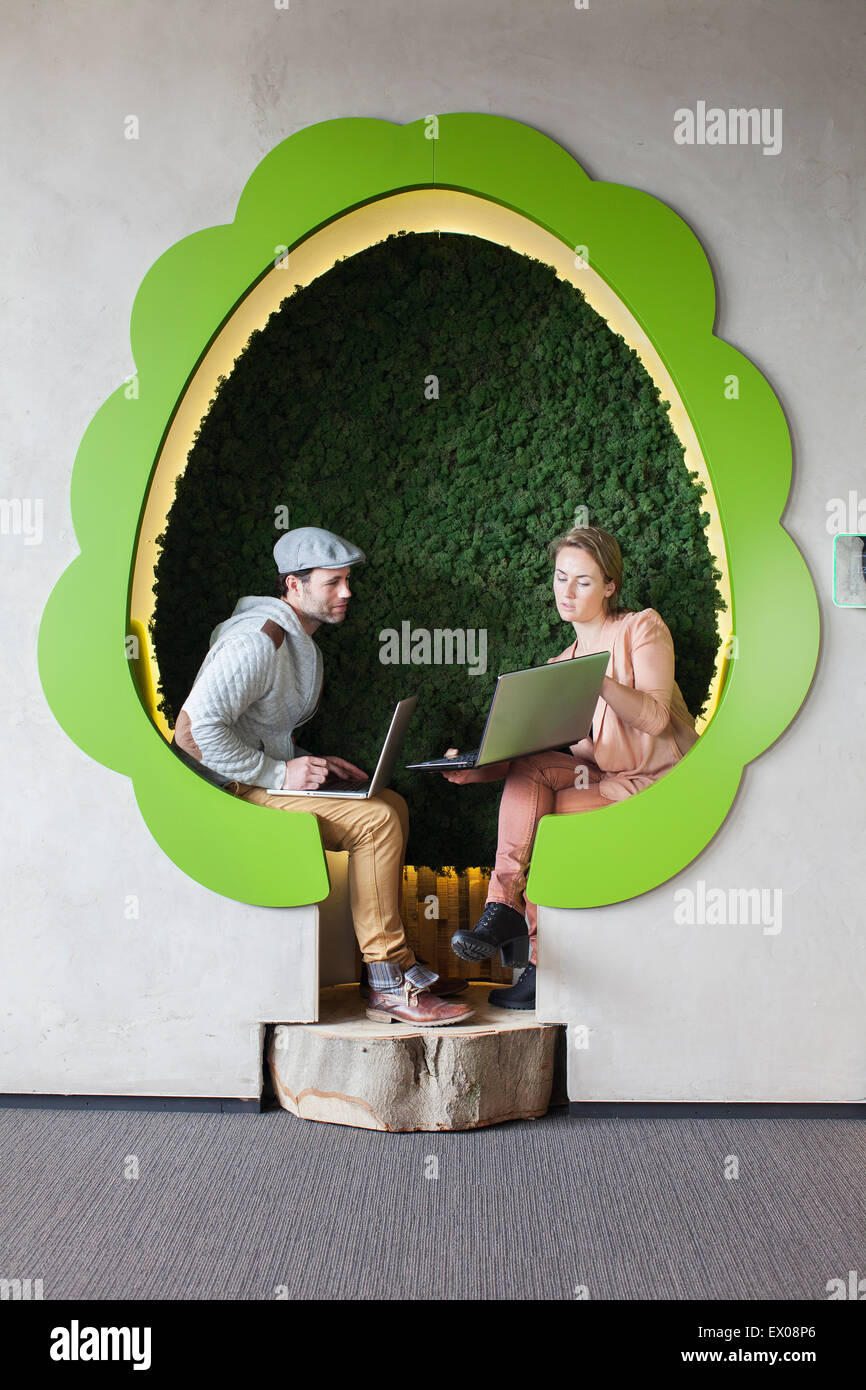 Männliche und weibliche Designer arbeiten auf Laptops im Baum geformt Büroflächen Stockfoto