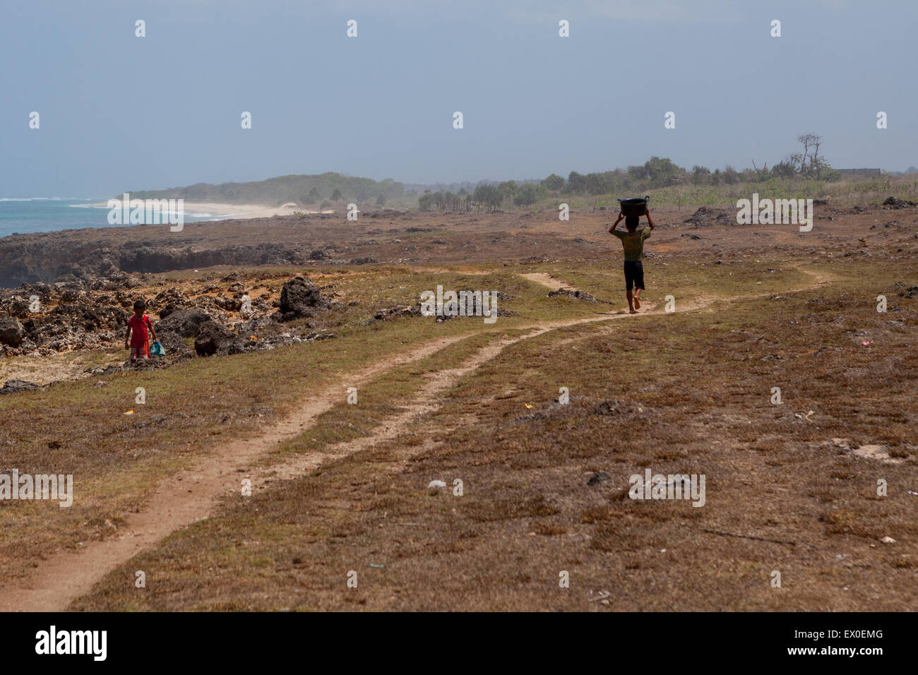 Ein Kind trägt einen Plastikeimer auf dem Kopf, während es auf trockenem Küstengelände in Pero, Pero Batang Villlage, Kodi, Südwest Sumba, Indonesien, läuft. Stockfoto