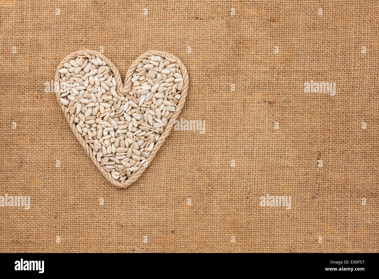 Herz aus Seil mit Sonnenblumenkernen liegen auf Sackleinen, mit Platz für text Stockfoto
