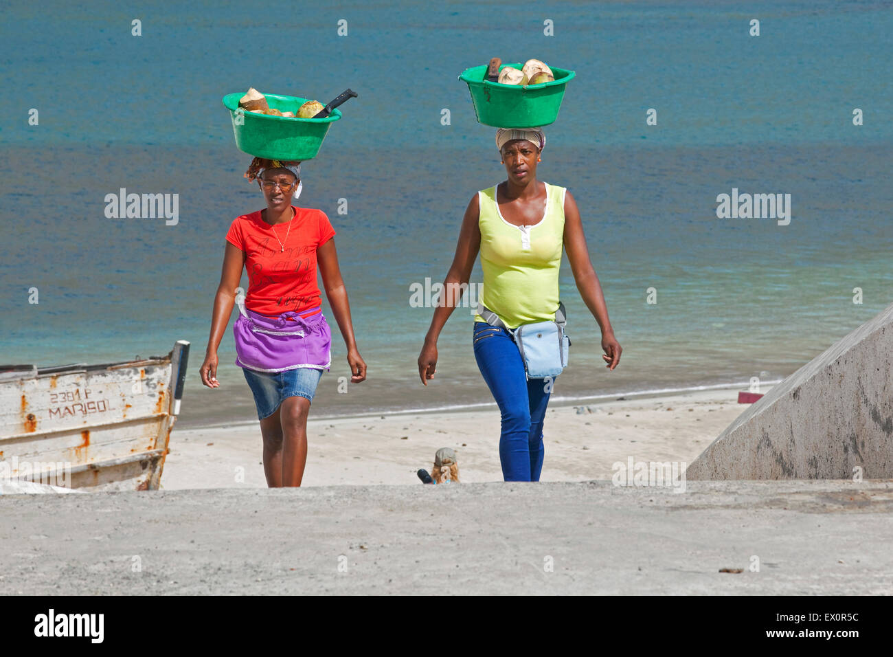 Zwei kreolische Frauen tragen Plastikwannen mit Kokosnüssen aus dem Hafen von Tarrafal auf der Insel Santiago, Kapverden, Afrika Stockfoto