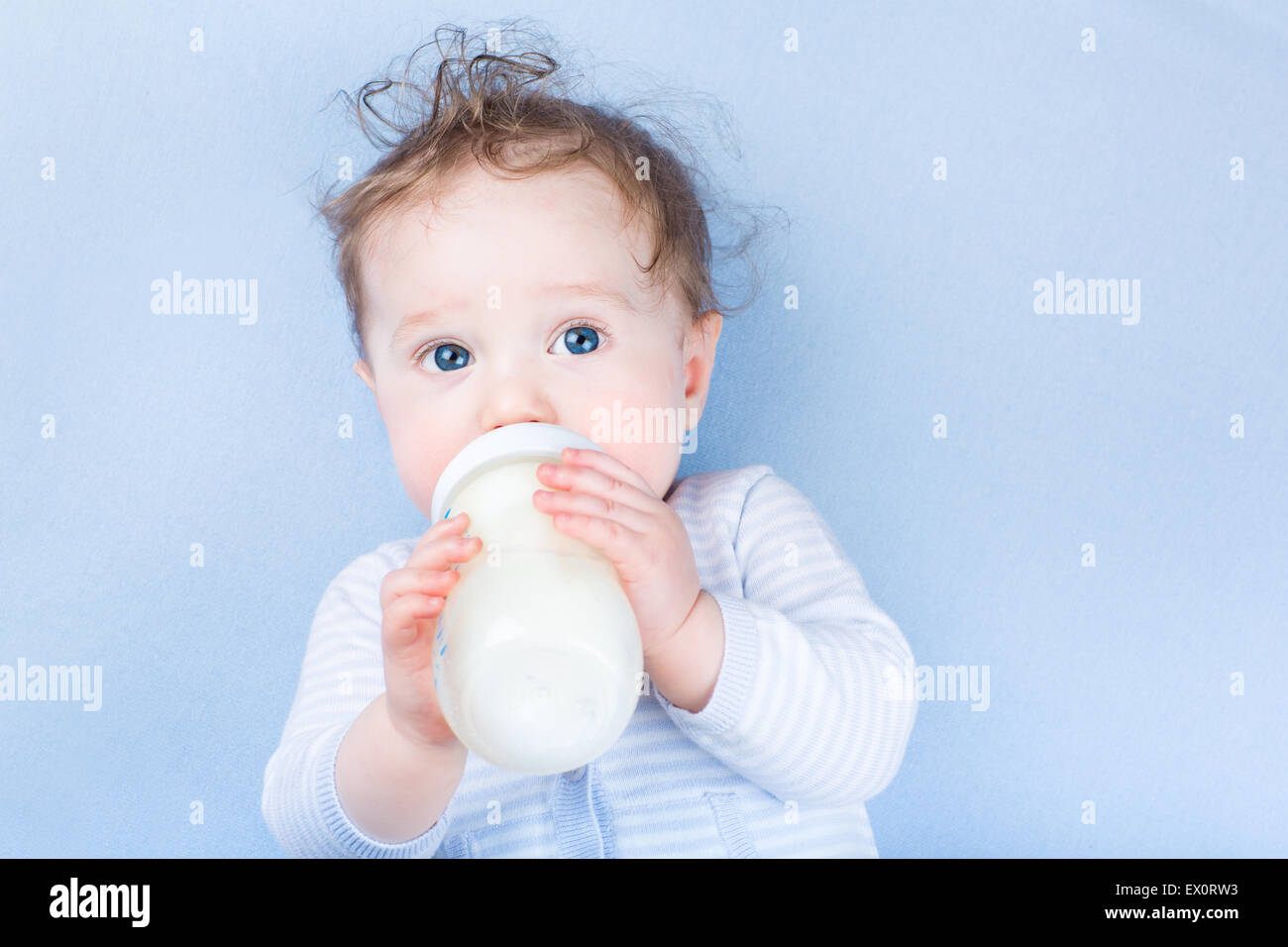 Süßes kleines Baby mit schönen blauen Augen Trinkmilch in einer Plastikflasche entspannend auf einer blauen gestrickte Decke Stockfoto