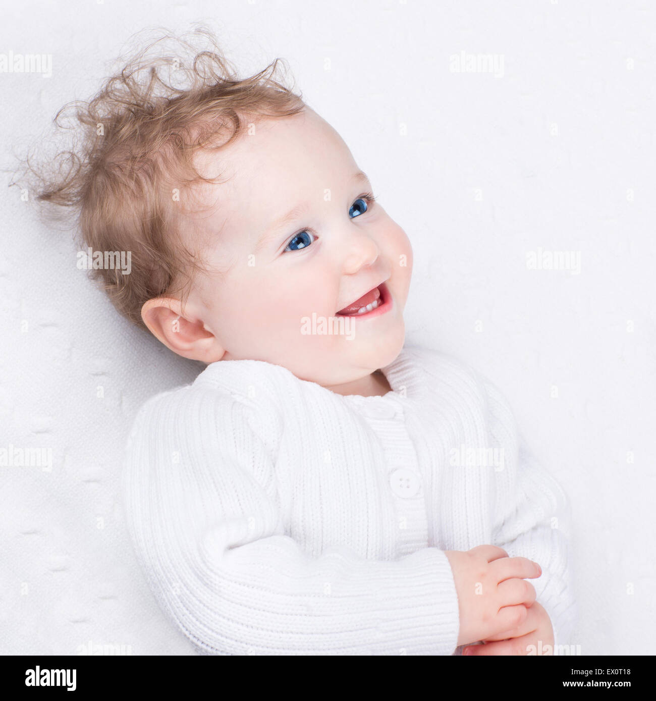 Liebenswert lachendes Baby tragen eine warme Strickjacke auf einer weißen Decke Stockfoto