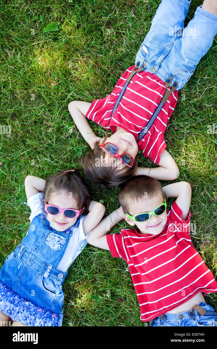 Glückliche fröhliche lächelnde Kindern, Verlegung auf einem Rasen, Sonnenbrille, lächelnd in die Kamera von oben geschossen Stockfoto