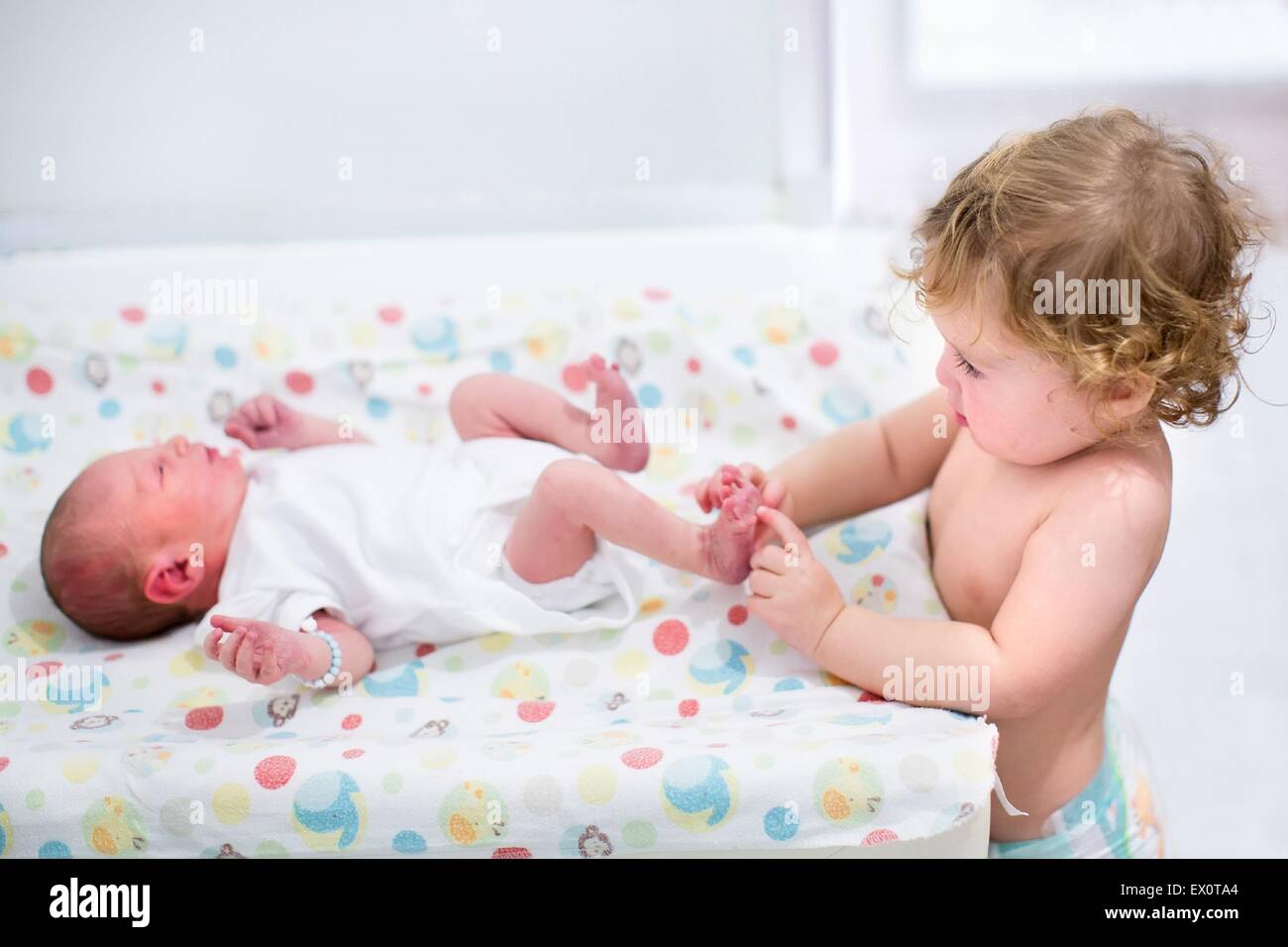 Porträt von einem niedlichen lockiges Kleinkind Mädchen spielen mit den Füßen des Bruders neugeborenes Baby auf einem Wickeltisch Stockfoto