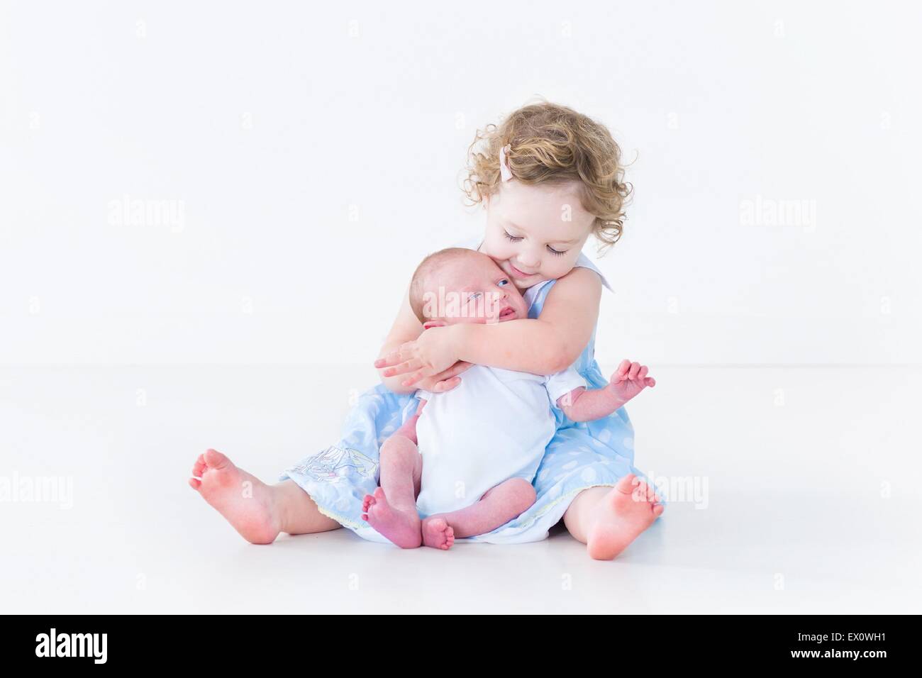 Süßes Kleinkind Mädchen in einem blauen Kleid ihr neugeborenes Baby Bruder küssen Stockfoto