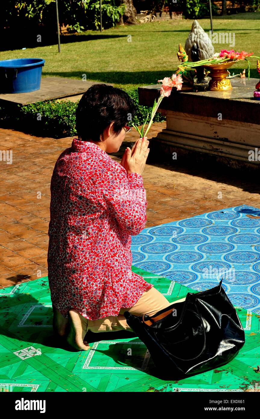 Chiang Mai, Thailand:: Thai Frau mit einem Stamm von Gladiola Blumen kniet im Gebet auf einem Outdoor-Schrein von Wat Phra Singh Stockfoto