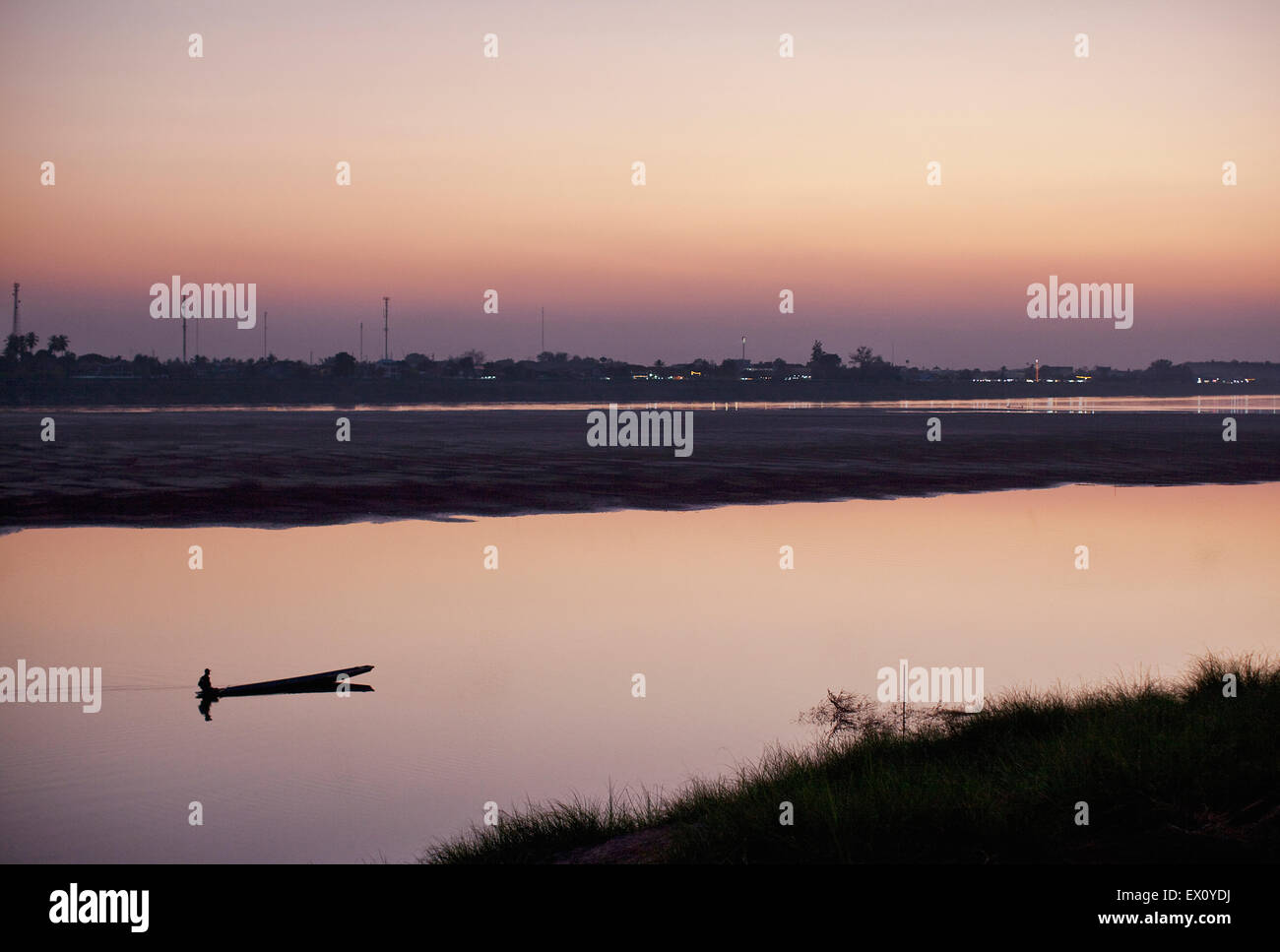 Ein Mann fährt ein Boot auf dem Mekong in der Abenddämmerung, während die Lichter von Thailand im Hintergrund, Vientiane, Laos gesehen werden kann Stockfoto