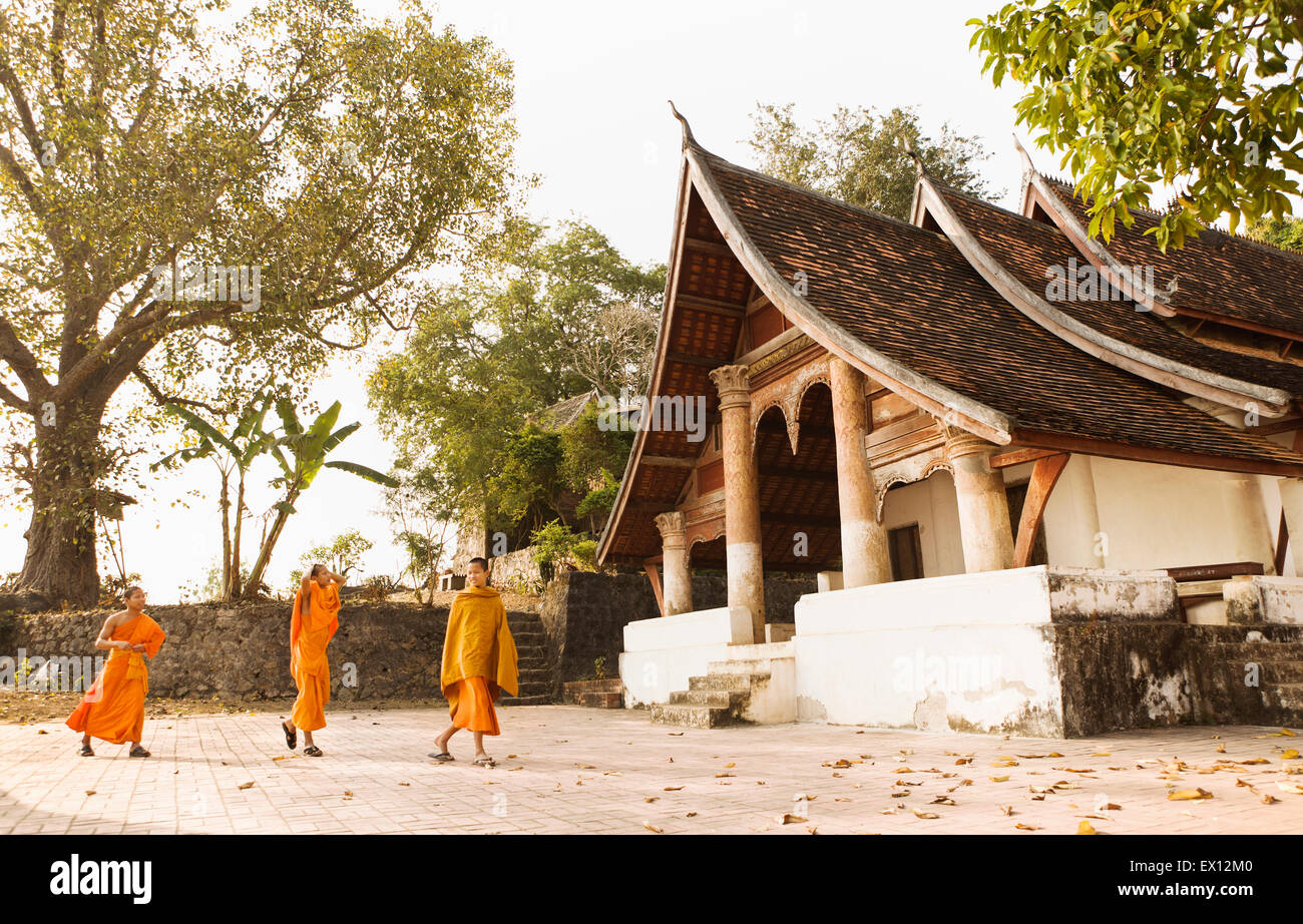Junge Mönche gehen von Wat Siphoutthabat Thipphuramm in der Morgendämmerung. Luang Prabang, Laos. Stockfoto